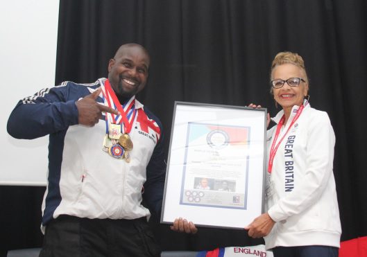 Olympians visit Fairfax Academy: Anita Neil, the first Black woman to represent Great Britain at an Olympic Games, is presented with a surprise world record certificate by top discus thrower and Fairfax staff member Kevin Brown.